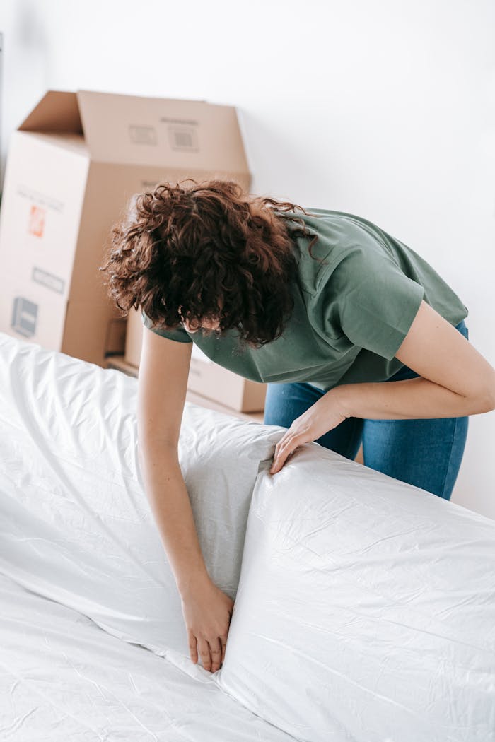 Woman covering a sofa with white cloth during a move, symbolizing protection and packing in a bright home environment.