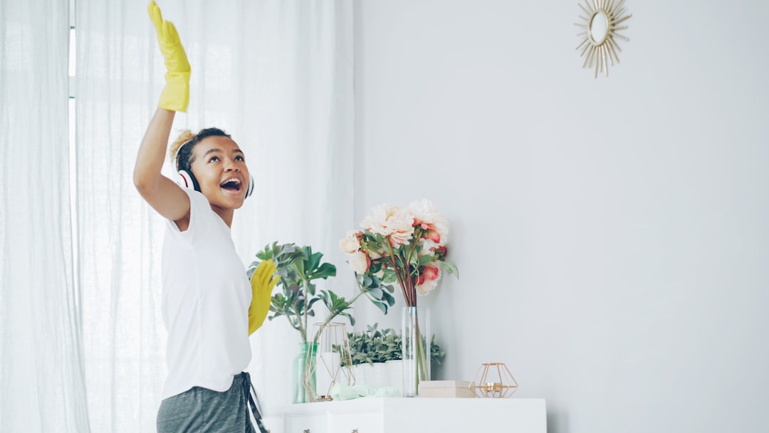 journey-02 Pretty African American housewife is dusting the furniture and enjoying music wearing wireless headphones, dancing and singing. Happy young woman is having fun and doing housework.
